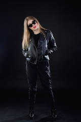 young girl in a black leather jacket and sunglasses on a dark background standing
