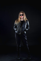young girl in a black leather jacket and sunglasses on a dark background standing