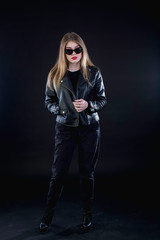 young girl in a black leather jacket and sunglasses on a dark background standing