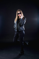 young girl in a black leather jacket and sunglasses on a dark background standing