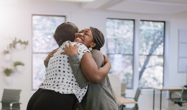 Two female black african freelancers embraced in a friendly hug in a modern co-working space