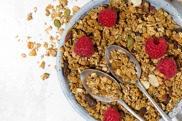 sweet granola on the plate and fresh raspberries on white table, top view closeup