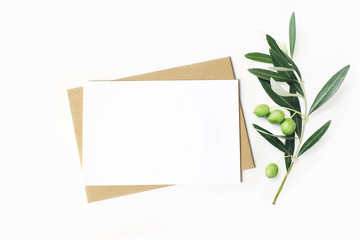 Feminine stationery, desktop mock-up scene. Blank horizontal greeting card and craft envelope with olive branch.White table background. Flat lay, top view.