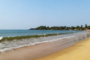 Wave on the sandy beach against the blue sky and jungle.