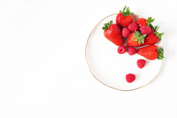 Styled stock food photo. Summer healthy fruit composition with red strawberries, raspberries on porcelain golden rim plate. White table background. Empty space. Flat lay, top view.
