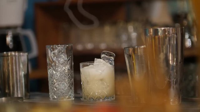 Young professional bartender pouring white crem drink into the glass full of ice and putting a pickle on it