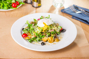 Green Vegetable Salad with tuna and Poached Egg on the white plate on the wooden served table. Selective focus, copy space.