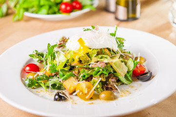 Close up Green Vegetable Salad with tuna and Poached Egg on the white plate on the wooden served table. Selective focus, copy space.