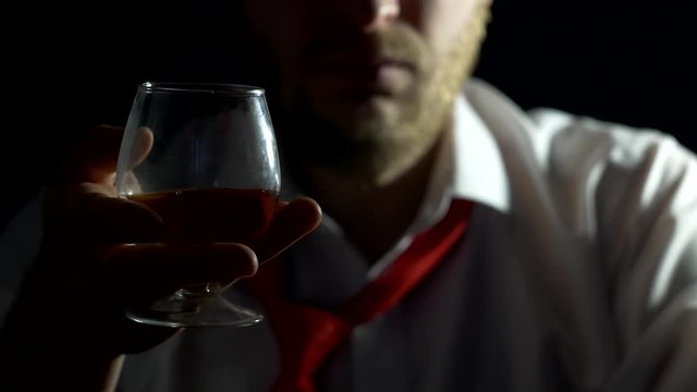 A man with a beard is sitting and holding a glass with alcohol in his hand, close-up, black background, copy space, concept