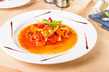 Close up stew fish fillet with vegetables decorated with basil leaf on the white plate on the served woodan table. healthy food, delicious lunched. Selective focus.