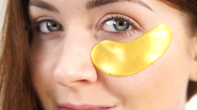 Young woman with golden collagen patches under eyes, closeup. Mask for removing wrinkles and dark circles. Girl taking care of delicate skin around eye. Beauty treatment