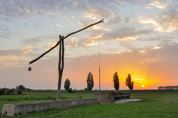 Fototapeta na wymiar Traditional water well (well sweep or shadoof) in Serbia with a beautifull sunset