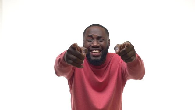 Slow motion attractive african american male pointing fingers you camera, laughing out loud mocking, joking indicating clumsy funny friend, bending chuckle touching knees, covering eyes giggling