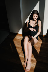 Fototapeta premium Waiting baby. Pregnant woman sitting near window and hands embraces a round belly, stomach. close-up. nine months. Baby Shower. Motherhood concept. front view.