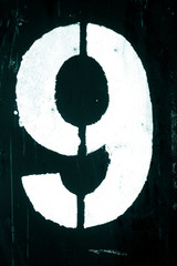 Number 9 in stencil on metal wall in cyan tone.
