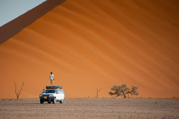 Fototapeta na wymiar Two Asian man traveler and photographer standing and sitting on camper car near orange sand dune. Travel desert concept