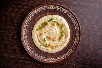 The concept of Arabic cuisine. Oriental hummus with grilled sesame and pistachios. A dish in a restaurant in a red ceramic dish on a wooden table. Top view, copy space