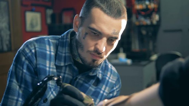 Tattooed male master is doing a tattoo by himself