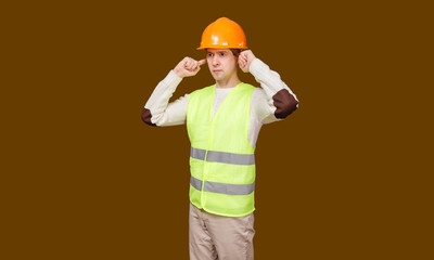 The young man in a construction helmet, a vest closed ears hands not to hear noise