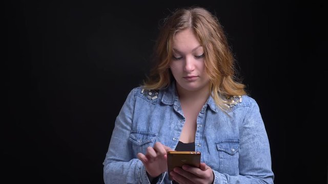 Closeup portrait of adult caucasian female texting on the phone with excitable smile with background isolated on black