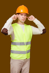 The young man in a construction helmet, a vest closed ears hands not to hear noise