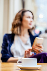 cup of tea on the table and a woman with a smartphone in the blur zone