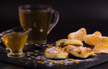 Cheesecakes with raisins, tangerine chips and powdered sugar. Next are slices of mandarin, honey and a cup of green tea