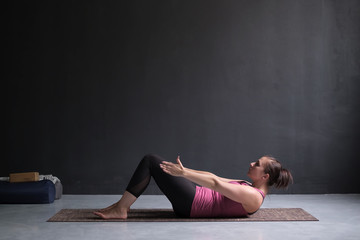 Young woman practicing yoga asana Ardha Navasana exercise at the yoga studio