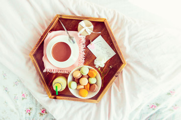 Breakfast in bed with empty blank card. Cup of coffee, juice, macaroons, rose flower and giftbox on wooden tray. Romantic breakfast in bed. Birthday, Valentine's day morning. Top view. Copy space.