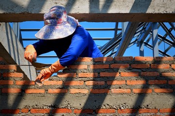 Sunlight and shadow on surface of female bricklayer in blue long sleeve t-shirt with hat is working to build brick wall inside building structure in construction site