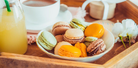 Sweet romantic breakfast in bed for lover. Close up macaroons, cup of coffee, juice, flower and gift box on wooden tray. Birthday, Valentine's day morning. Wide banner. Selective focus.