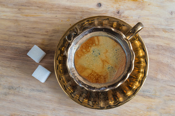 Coffee break concept: beautiful golden cup of coffee and two sugar on the wooden background top view