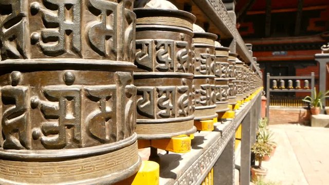 Row of aged religious prayer wheels or drums with mantra Om Mani Padme Hum in yard of temple, Durbar Square, Nepal, Kathmandu. Tibetian buddhism
