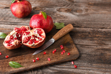 Cutting board with ripe pomegranates and knife on wooden table