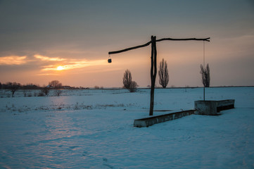 Fototapeta na wymiar Traditional water well (well sweep or shadoof) during the winter in Serbia with a beautifull sunset