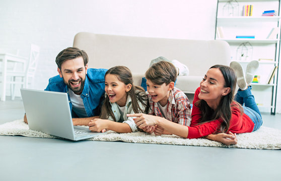 Beautiful modern young family lying on the floor at home and doing something in laptop