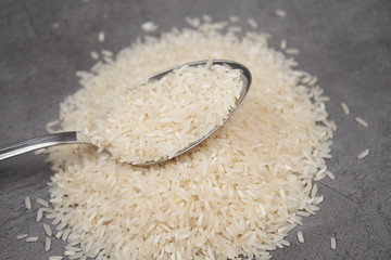 Raw rice basmati slide with a spoon on a dark background close-up 
