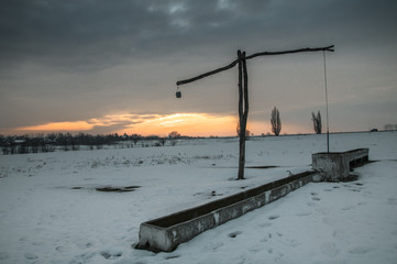 Traditional water well (well sweep or shadoof) during the winter in Serbia with a beautifull sunset