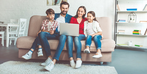 Happy beautiful family with laptop on the couch at home in casual clothes