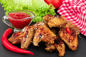 Baked chicken wings with sesame seeds and sweet chili sauce on dark background