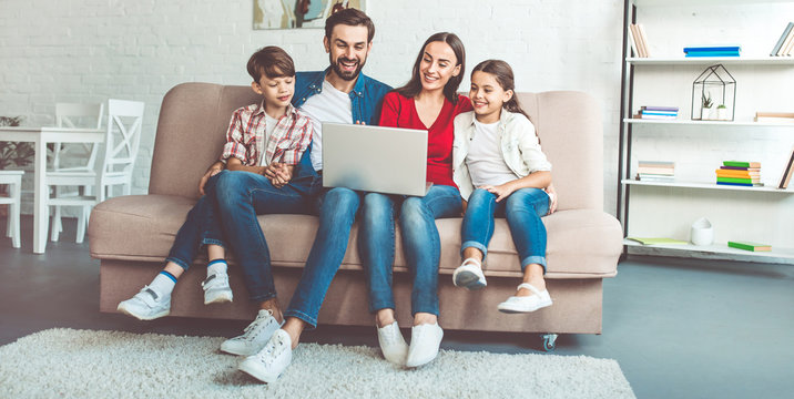 Happy Beautiful Family With Laptop On The Couch At Home In Casual Clothes