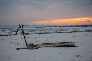 Traditional water well (well sweep or shadoof) during the winter in Serbia with a beautifull sunset