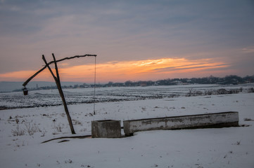 Traditional water well (well sweep or shadoof) during the winter in Serbia with a beautifull sunset