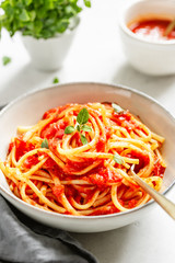 Traditional pasta with tomato and Greek basil sauce in a ceramic bowl on a white table.