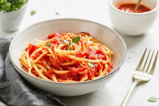 Traditional pasta with tomato and Greek basil sauce in a ceramic bowl on a white table.