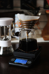 Alternative manual coffee brewing with paper filter in stainless steel dripper. On the electronic scale. Manual grinder