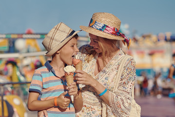 Cute European boy and his mother are walking around the amusement park and eating tasty ice-cream.