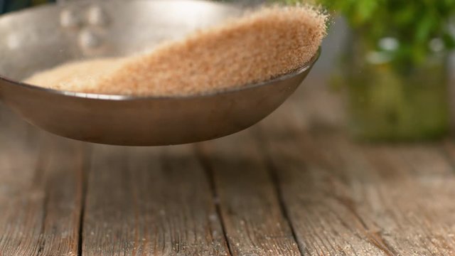 SLOW MOTION, MACRO, DOF: Brown breadcrumbs fall onto the wooden table while being toasted in a hot metal pan. Unrecognizable chef roasting grated bread and crackers over a rustic kitchen counter.