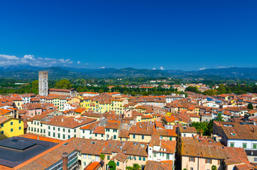 Fototapeta na wymiar Aerial top panoramic view of Piazza dell Anfiteatro square, Chiesa di San Frediano church in historical centre medieval town Lucca with terracotta tiled roofs, green hills background, Tuscany, Italy