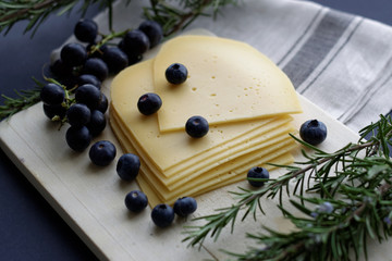 Sliced dutch cheese on wooden cutting board with fresh rosemary , grapes and blueberries